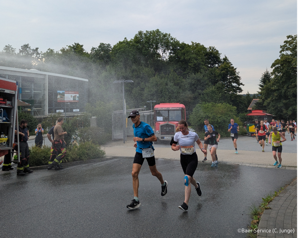 Läufer laufen durch einen Wasserstrahl von der Feuerwehr auf der Strecke zur Abkühlung beim 21. Sparkassen-Festungslauf Königstein