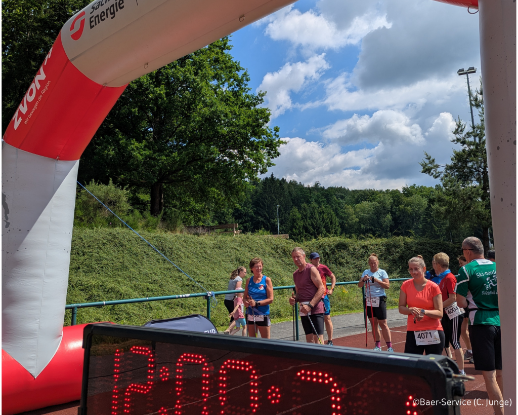 Einzelne Läufer versammeln sich an der Startlinie, im Vordergrund ist eine Anzeigetafel mit Uhrzeit (3. Sebnitzer Hirsch-Cross-Challange)